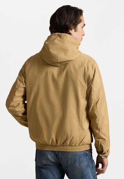 Khaki hooded jacket with elastic cuffs and waistband. Smooth material and relaxed fit. Back view shows seams and soft texture.
