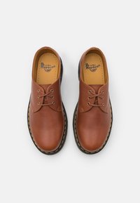 Paire de chaussures en cuir marron Dr. Martens avec des semelles noires et des coutures jaunes, vues de dessus sur un fond blanc.