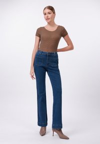 Brown striped fitted t-shirt paired with high-waisted dark blue flared jeans featuring front and back pockets, worn with pointed beige heels.