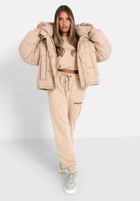 Beige pufferjacka med quiltat mönster, tillsammans med matchande kort sweatshirt och sweatpants. Den avslutande touchen är ljusgrå sneakers.