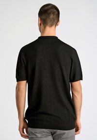 Svart kortärmad stickad polo med ribbat krage och manschetter, har en slät yta och en skräddarsydd passform.