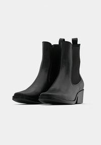 Černé kotníkové boty vyrobené z hladké kůže s mírným podpatkem, elastickými bočními panely a poutky pro snadné obouvání.
