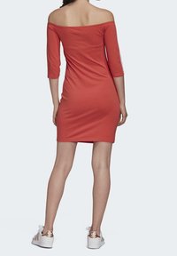 Rode off-shoulder jurk met driekwart mouwen, strakke pasvorm, zachte textuur, en gecombineerd met witte sneakers met gouden accenten.