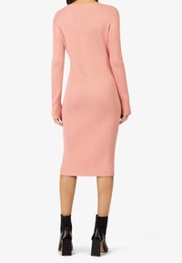 Femme portant une robe midi rose ajustée à manches longues côtelées, associée à des bottines à talons noires, vue de dos.