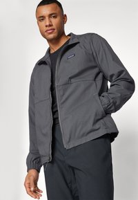 Grey jacket made of lightweight fabric, featuring a zip front, two large pockets, and elasticized cuffs. Patagonia logo on the chest.