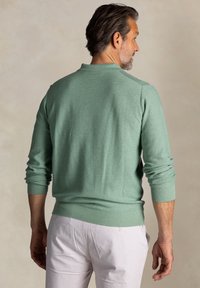 Groene gebreide pullover met een geribde kraag en manchetten, met lange mouwen en een aangesloten zoom. Draag het met lichtgekleurde broeken.