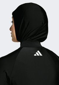 Sort atletisk langærmet top med påhæftet hætte, med en hvid Adidas-logo på ryggen. Glat, let stofstruktur.