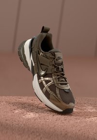 Braune Mesh- und Kunstmaterial-Sneaker mit einer dicken weißen Sohle, ausgestattet mit metallischen Akzenten und einem auffälligen Nike-Logo an der Seite.