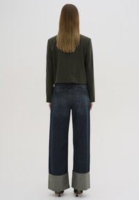 Veste cropped vert olive à manches longues associée à un pantalon large en denim sombre taille haute avec des poignets gris contrastants.