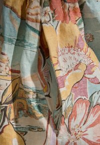 Colorful fabric with large floral and scenic patterns in shades of yellow, pink, green, and blue, shown in soft folds and texture.