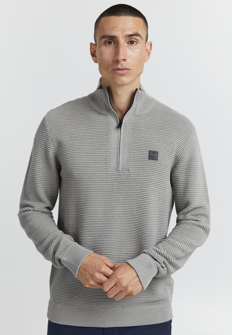 Lys grå genser med kvart glidelås, som har vertikal ribbet tekstur og et lite logo-patch på brystet. Slim-fit design.