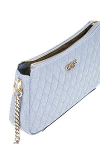 Sac synthétique matelassé bleu clair avec une fermeture éclair dorée, une bandoulière chaîne et un logo en relief. Forme rectangulaire avec une texture lisse.