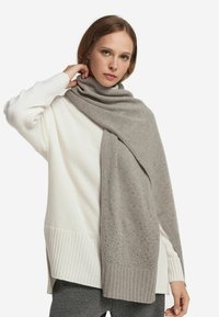 Szary dzianinowy szalik z teksturowanymi detalami spoczywa na miękkim białym swetrze z prążkowanymi akcentami, uzupełnionym luźnym krojem.