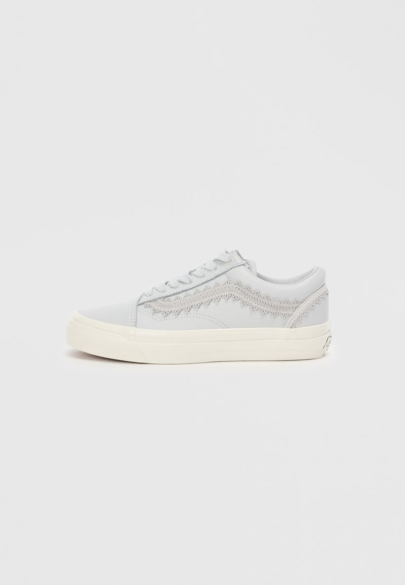 Adidași gri cu un design texturat, talpă din cauciuc alb și șireturi plate. Prezintă cusături decorative pe părțile laterale. Stil minimalist.