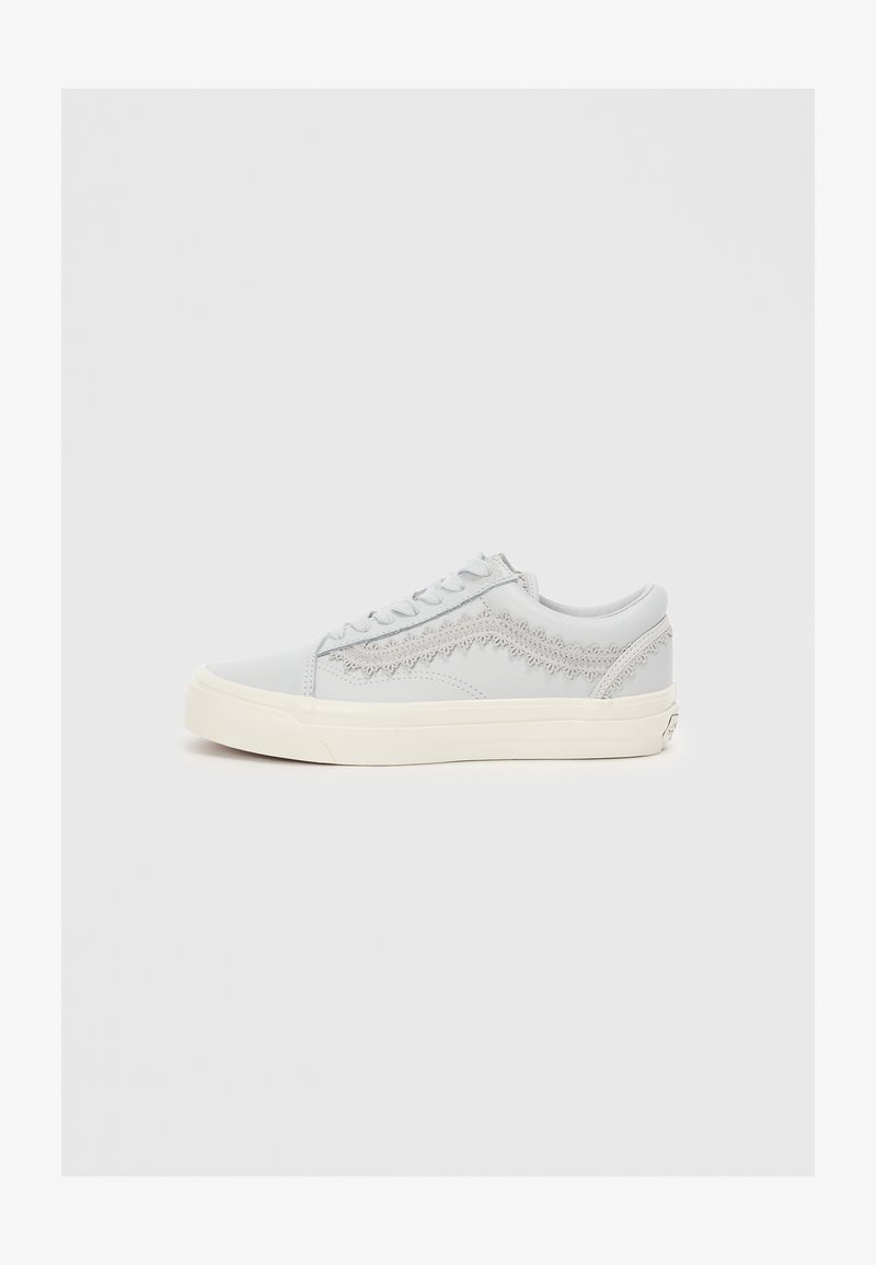 Szare sneakersy z teksturowanym wzorem, białą gumową podeszwą i płaskimi sznurówkami. Ozdobne przeszycia wzdłuż boków. Styl minimalistyczny.