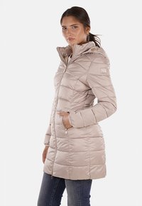 Cappotto imbottito trapuntato beige chiaro, con cappuccio, zip frontale e tasche. Texture simile alla satinata con una leggera lucentezza e un marchio discreto sulla manica.