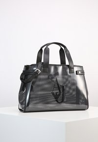 Černá perforovaná taška s pevnými černými uchy a odnímatelným ramenním řemínkem. Má hladkou texturu a jemný detail loga.