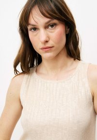 Helles beige ärmelloses Oberteil mit strukturiertem Oberflächen, das vertikale Linien und subtile Paillettendetails für einen schimmernden Effekt aufweist.