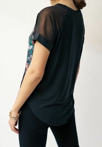 Černé tričko s krátkým rukávem a průhlednými rukávy; na přední straně je barevný květinový vzor. Měkká tkanina s volným střihem a zaobleným lemem.