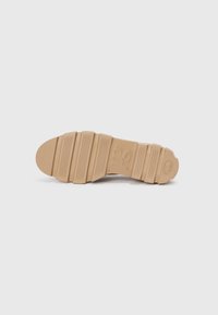 Semelle en caoutchouc beige avec un motif texturé ; présente des rainures horizontales et un emblème circulaire au niveau du talon pour favoriser la traction et le soutien.