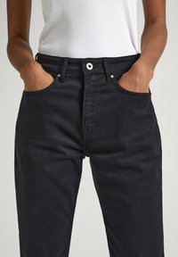 Jeans de mezclilla negra con cinturilla alta, que cuentan con bolsillos delanteros y un diseño clásico de cinco bolsillos. Textura suave y cierre de botón estándar.