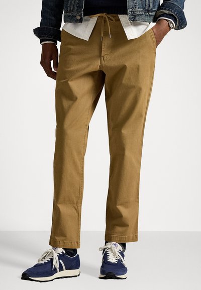 Pantalons en coton brun clair avec une coupe décontractée, dotés d'une taille à cordon, de poches latérales et associés à des baskets bleu marine.