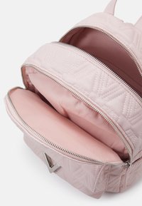 Vadderad rosa ryggsäck med silverfärgade dragkedjor, som har två fack klädda med mjuk tyg. Noterbart chevronmönster på utsidan.