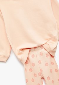 Bluzka w kolorze brzoskwiniowym zestawiona z prążkowanymi legginsami w różowy kwiatowy wzór.