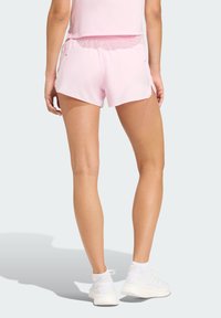 Pink athletic shorts with a relaxed fit, featuring a drawstring waist, side slits, and smooth fabric. Worn with white sneakers.