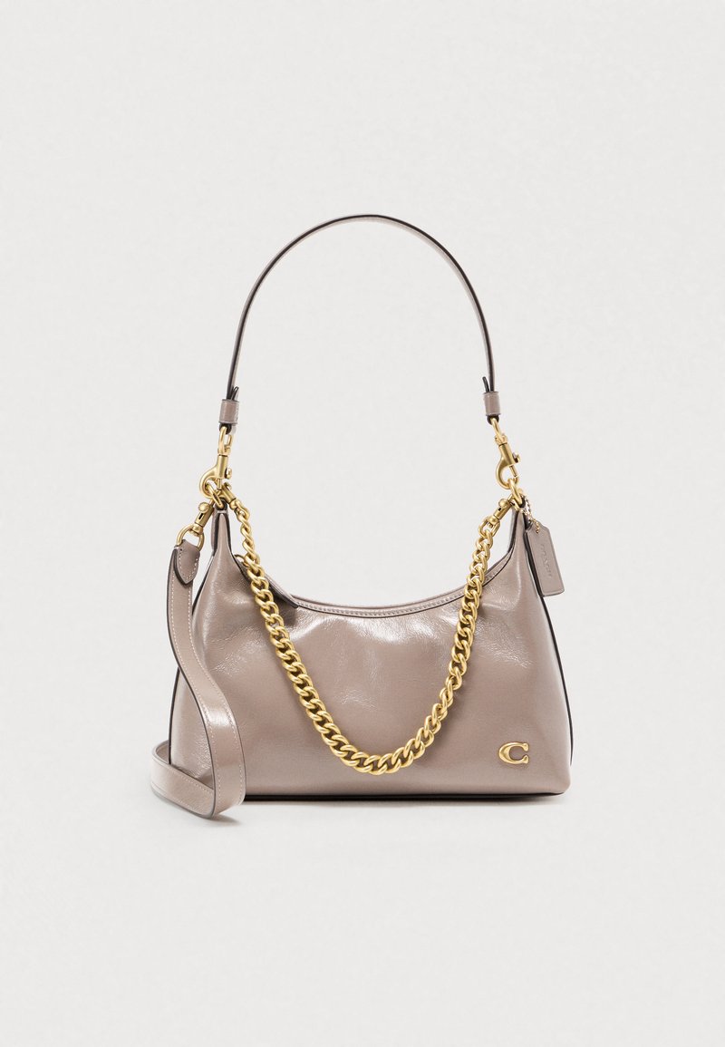 Χειροποίητη τσάντα ώμου από ανοιχτό μπεζ δέρμα με γυαλιστερό φινίρισμα, χρυσή αλυσίδα ιμάντα και αντίθετη σκούρα λαβή, με μικρό λογότυπο στο μπροστινό μέρος.