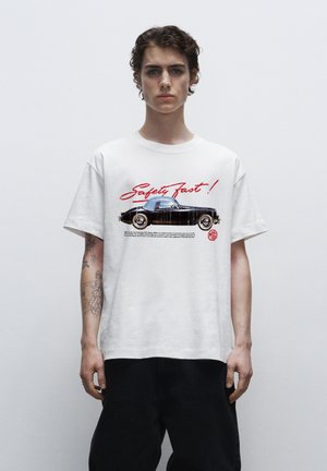 Hvid bomulds t-shirt med et sort vintage bil grafik og rød "Safety Fast!" tekst, korte ærmer og en afslappet pasform.