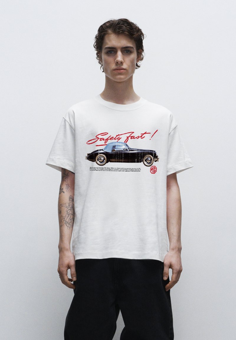 Vit bomull t-shirt med en svart vintage bilgrafik och röd text "Safety Fast!", korta ärmar och en avslappnad passform.