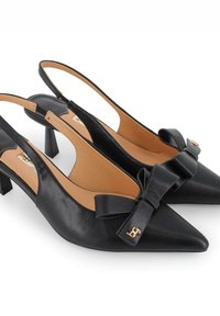 Zapatos de tacón slingback de cuero negro con punta afilada, que cuentan con un acento de lazo y un pequeño detalle de hardware dorado en el costado. Tacón cuadrado moderado.