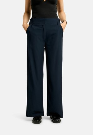 Pantalon à jambes larges de couleur bleu marine, fabriqué en tissu lisse. Il présente une taille haute et des poches latérales. Stylisé avec un haut noir et des chaussures assorties.
