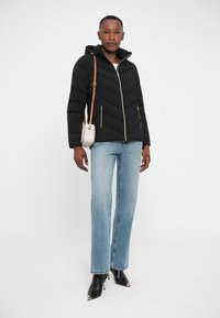 Doudoune noire avec des coutures en chevrons, poches zippées et capuche, associée à un jean bleu clair et des bottes à talons noires.