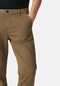 Slim-fit brązowe bawełniane spodnie z bocznymi kieszeniami i zapięciem na guzik. Gładka tekstura, zorganizowany design, dopasowany krój w okolicy talii i ud.