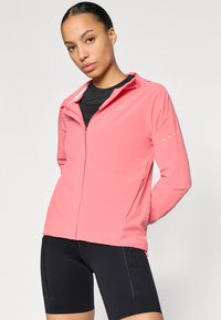 Ελαφρύ, μπουφάν με φερμουάρ σε ζωντανό ροζ ύφασμα, με κουκούλα, ανακλαστικό λογότυπο και μινιμαλιστικές λευκές λεπτομέρειες στα μανίκια.