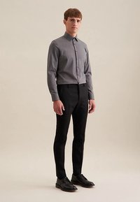 Grijs overhemd met knopen en een spitse kraag, gecombineerd met zwarte broek. Het overhemd heeft een gladde textuur en een slanke pasvorm. Zwarte schoenen.