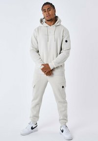 Sudadera con capucha en gris claro, con un bolsillo tipo canguro, combinada con pantalones cargo a juego que cuentan con bolsillos laterales y un botón negro de acento.