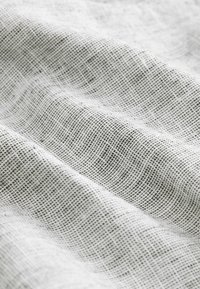 Tissu en lin gris clair avec une surface texturée, présentant un motif fin en grille et une apparence douce et fluide.