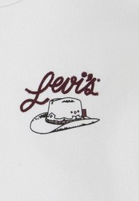 O logótipo da Levi's em bordado bordeaux apresenta um chapéu de cowboy sobre um fundo de tecido branco. O design inclui um contorno detalhado do chapéu e realces.