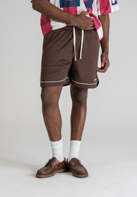 Pantaloni scurți din plasă maro cu margini albe �și șnur. Purtați cu ciorapi albi și pantofi maronii. Designul include tăieturi laterale pentru confort.