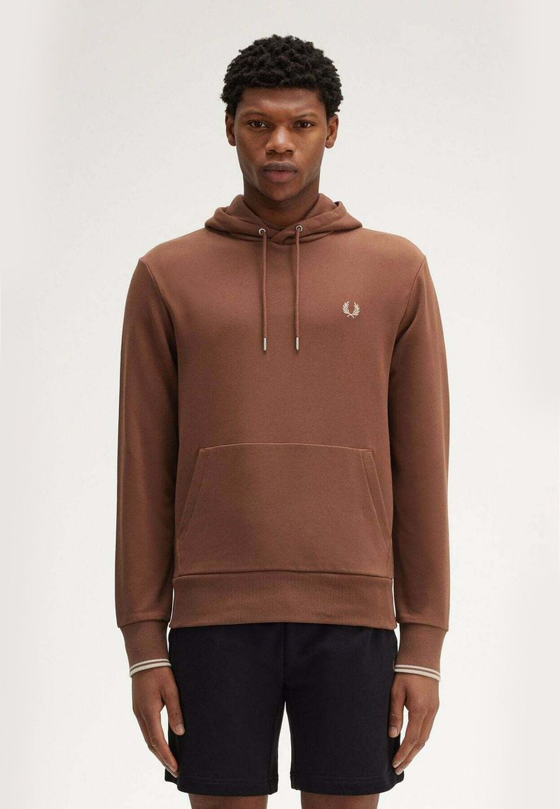 Felpa marrone con tasca frontale, cappuccio regolabile e polsini a coste. Presenta un piccolo logo sul petto. Abbinata a pantaloni corti scuri.