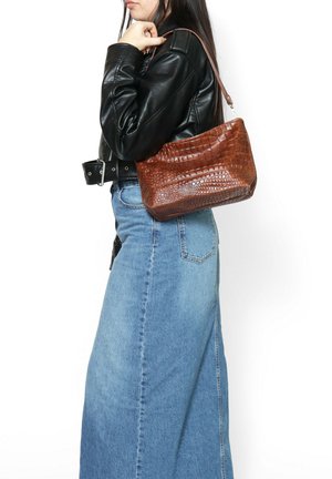 Borsa in pelle marrone con effetto coccodrillo, dalla forma curvata e con una sola tracolla, indossata con una gonna di denim e un giubbotto in pelle.