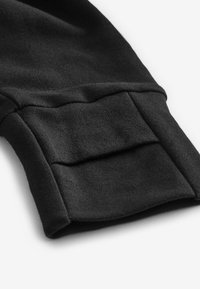 Poignet de sweat-shirt noir avec une texture lisse, présentant un design plié et un détail de couture subtil, avec une poche fonctionnelle.