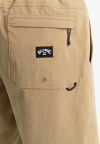 Bermudas cargo color caqui con un patrón de cuadrícula texturizado, que cuentan con un bolsillo trasero con cremallera, un parche con el logo y un detalle de asa.