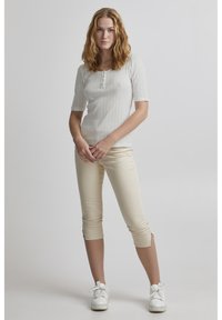 Lys grå, kortærmet top med et struktureret mønster og en knaplukning. Kombineret med beige cropped bukser og hvide sneakers.