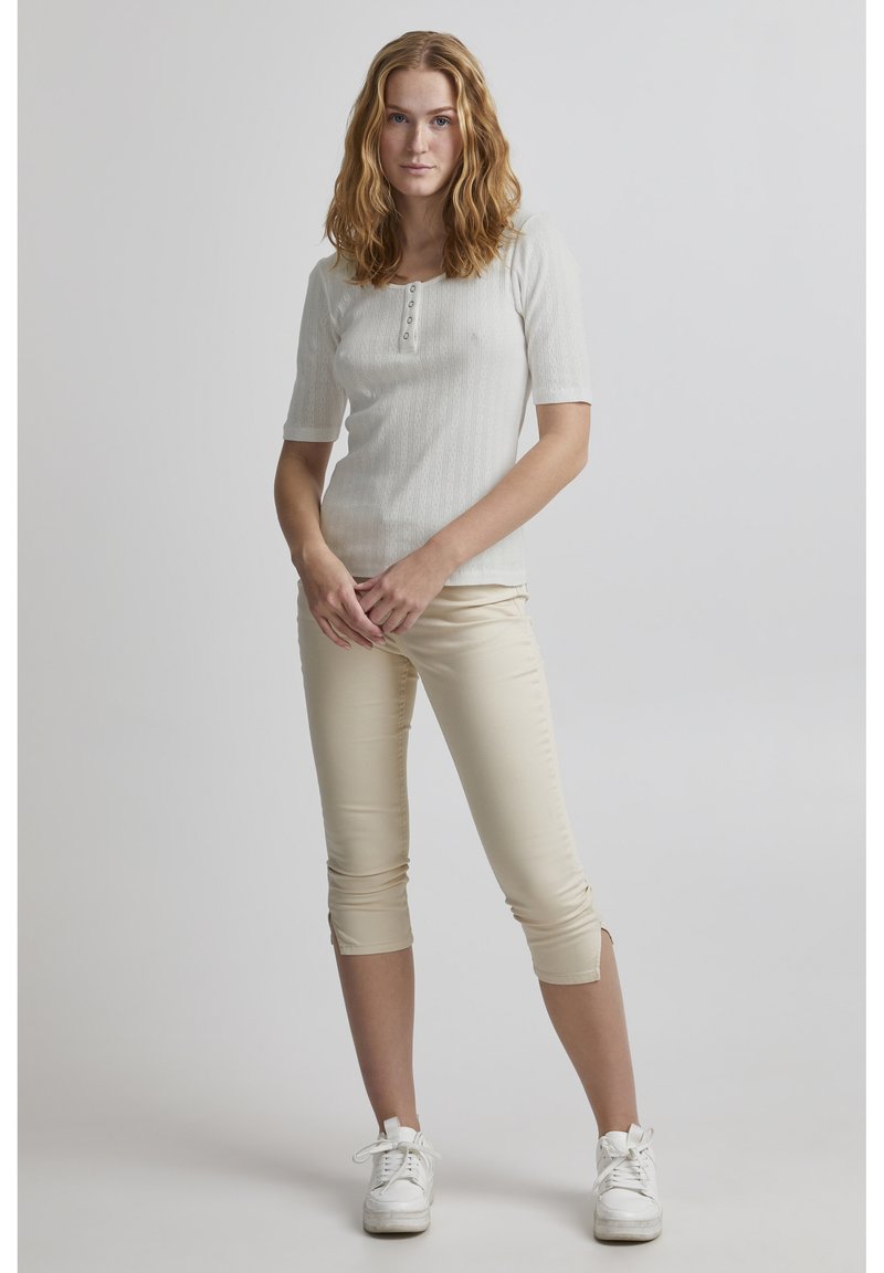 Lys grå, kortærmet top med et struktureret mønster og en knaplukning. Kombineret med beige cropped bukser og hvide sneakers.