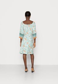 Blommig klänning i ljusblått med orange detaljer; har trekvartsärmar och fyrkantig axelringning, medellång och utsvängd form.