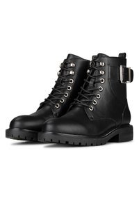 Stivaletti neri in pelle con lacci alla caviglia, dotati di suola spessa con incavi e dettaglio in fibbia argentata sul lato, angolati per mostrare entrambe le scarpe.